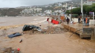 Petugas pemadam kebakaran dan warga melihat kerusakan akibat bannir bandang yang melanda di desa Agia Pelagia,  Pulau Kreta, Yunani, Sabtu (15/10/2022). [Costas METAXAKIS / AFP]