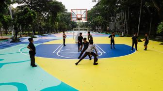 Anak-anak bermain basket di atas mural karya seniman grafiti Stereoflow alias Adi Dharma di Lapangan Taman Menteng, Jakarta Pusat, Rabu (18/10/2022). [Suara.com/Alfian Winanto]