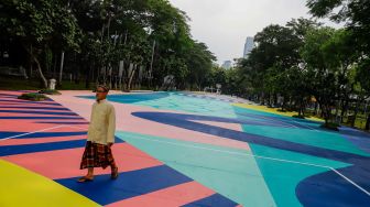 Warga berjalan di atas mural karya seniman grafiti Stereoflow alias Adi Dharma di Lapangan Taman Menteng, Jakarta Pusat, Rabu (18/10/2022). [Suara.com/Alfian Winanto]