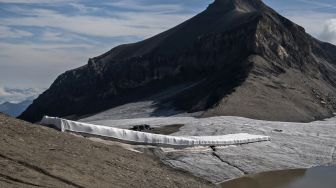 Pekerja berusaha menyelimuti es di celah Tsanfleuron untuk mencegahnya mencair di resor Glacier, Les Diablerets, Swiss, Selasa (13/9/2022). [Fabrice COFFRINI / AFP]
