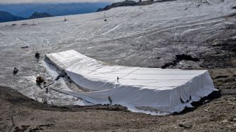 Pekerja berusaha menyelimuti es di celah Tsanfleuron untuk mencegahnya mencair di resor Glacier, Les Diablerets, Swiss, Selasa (13/9/2022). [Fabrice COFFRINI / AFP]
