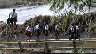 Sejumlah siswa dan warga berjalan di jembatan beton yang ambruk saat berangkat ke sekolah pascabanjir bandang di Dusun Sekar Kejula Kelod, Desa Yehembang Kauh, Jembrana, Bali, Selasa (25/10/2022).  [ANTARA FOTO/Nyoman Hendra Wibowo/hp].