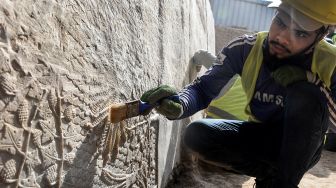 Seorang pekerja menggali relief pahatan batu yang baru-baru ini ditemukan di Gerbang Mashki, Kota Mosul, Irak, Rabu (19/10/2022). [Zaid AL-OBEIDI / AFP]
