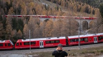 Warga mengambil gambar kereta api sepanjang 1910 meter dengan 100 gerbong saat melintas di dekat Bergun, Swiss, Sabtu (29/10/2022). [Fabrice COFFRINI / AFP]
