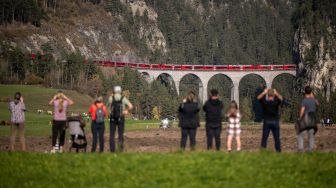 Warga mengambil gambar kereta api sepanjang 1910 meter dengan 100 gerbong saat melintas di dekat Bergun, Swiss, Sabtu (29/10/2022). [Fabrice COFFRINI / AFP]
