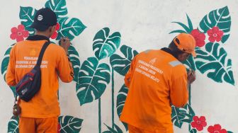 Petugas pasukan oranye wilayah Cipinang Melayu membuat mural motif bunga di kolong jalan tol Becakayu, Jatiwaringin, Jakarta Timur, Selasa (8/11/2022). [Suara.com/Alfian Winanto]