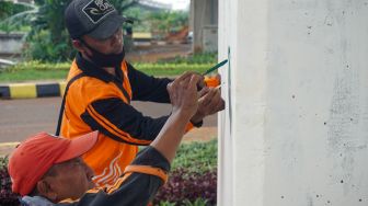 Petugas pasukan oranye wilayah Cipinang Melayu membuat mural motif bunga di kolong jalan tol Becakayu, Jatiwaringin, Jakarta Timur, Selasa (8/11/2022). [Suara.com/Alfian Winanto]