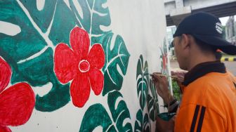 Petugas pasukan oranye wilayah Cipinang Melayu membuat mural motif bunga di kolong jalan tol Becakayu, Jatiwaringin, Jakarta Timur, Selasa (8/11/2022). [Suara.com/Alfian Winanto]