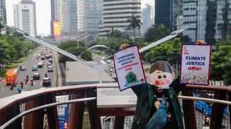 Aktivis Extinction Rebellion Indonesia (XR Indonesia) dan Walhi Jakarta melakukan aksi dengan membentangkan spanduk berisi kalimat sindiran untuk pelaksanaan KTT G20 di JPO Pinisi, Jakarta Pusat, Senin (14/11/2022). [Suara.com/Alfian Winanto]