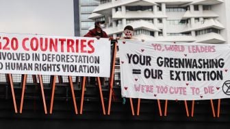 Aktivis Extinction Rebellion Indonesia (XR Indonesia) dan Walhi Jakarta melakukan aksi dengan membentangkan spanduk berisi kalimat sindiran untuk pelaksanaan KTT G20 di JPO Pinisi, Jakarta Pusat, Senin (14/11/2022). [Suara.com/Alfian Winanto]