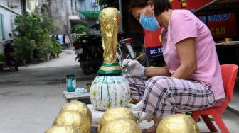 Seorang pekerja melukis model plester trofi Piala Dunia di sebuah lokakarya di Hanoi, Vietnam, Rabu (16/11/2022). [Nhac NGUYEN / AFP]