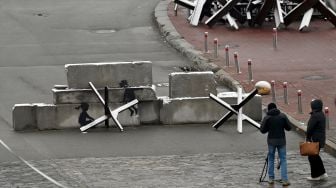 Seorang pria memfilmkan karya seniman jalanan Inggris Banksy di sebuah konstruksi anti-tank yang tertutup salju di Independence Square di Kyiv, Ukraina, Kamis (17/11/2022). [Sergei SUPINSKY / AFP]