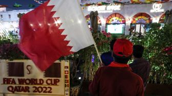 Seorang pria mengibarkan bendera Qatar saat menyaksikan pertandingan sepak bola Grup A Piala Dunia 2022 antara Qatar dan Ekuador di Souq Waqif di Doha, Qatar, Minggu (20/11/2022). [Giuseppe CACACE/AFP]