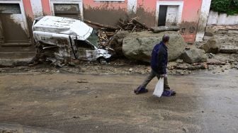 Seorang pria berjalan melewati mobil yang rusak akibat hujan lebat yang memicu tanah longsor di pulau Ischia selatan, Italia, Sabtu (26/11/2022). [Ciro FUSCO / Ansa / AFP]
