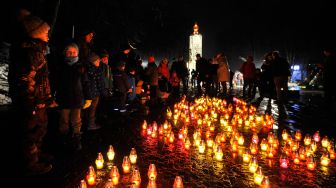 Penduduk lokal menyalakan lilin saat upacara di monumen korban Holodomor di Kyiv, Ukraina, Sabtu (26/11/2022). [Sergei CHUZAVKOV / AFP]