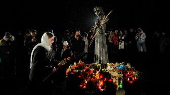 Seorang penduduk setempat meletakkan bunga saat upacara di monumen para korban Holodomor di Kyiv, Ukraina, Sabtu (26/11/2022). [Sergei CHUZAVKOV / AFP]
