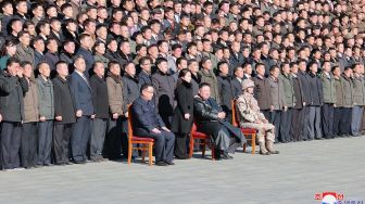 Pemimpin Korea Utara Kim Jong Un (duduk di tengah) dan putrinya (berdiri di tengah) foto bersama dengan para ilmuwan, insinyur, pejabat militer dan para pekerja di pabrik amunisi yang berkontribusi dalam uji coba rudal balistik antarbenua (ICBM) Hwasong-17 di lokasi rahasia, dalam foto tak bertanggal yang rilis pada Minggu (27/11/2022). [KCNA VIA KNS / AFP]