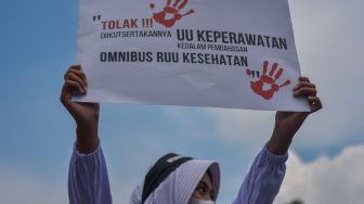 Seorang tenaga kesehatan membentangkan poster saat berunjuk rasa menolak RUU Omnibuslaw Kesehatan di depan Gedung Parlemen, Senayan, Jakarta, Senin (28/11/2022). [ANTARA FOTO/Sulthony Hasanuddin/wsj]