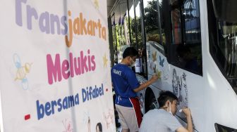 Dua anak berkebutuhan khusus melukis pada badan bus Transjakarta di Kantor Pusat Transjakarta, Cawang, Jakarta, Kamis (1/12/2022).[ANTARA FOTO/Darryl Ramadhan/nym].