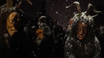 Orang-orang mengenakan topeng setan dan kulit domba hitam yang mewakili Krampus, penolong Santo Nikolas saat menghadiri parade Santo Nikolas (Nikolospiel) di Bad Mitterndorf, Styria, Austria, Senin (5/12/2022). [JOE KLAMAR / AFP]