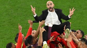 Para pemain Maroko melempar pelatih Walid Reragui ke udara saat mereka merayakan kemenangan pada akhir pertandingan sepak bola babak 16 besar Piala Dunia Qatar antara Maroko dan Spanyol di Education City Stadium di Al-Rayyan, barat Doha, Qatar, Selasa (6/12/2022). [Glyn KIRK / AFP]