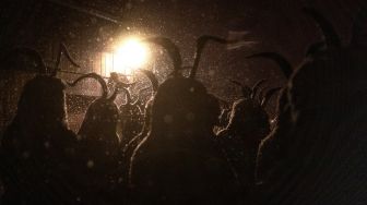 Orang-orang mengenakan topeng setan dan kulit domba hitam yang mewakili Krampus, penolong Santo Nikolas saat menghadiri parade Santo Nikolas (Nikolospiel) di Bad Mitterndorf, Styria, Austria, Senin (5/12/2022). [JOE KLAMAR / AFP]