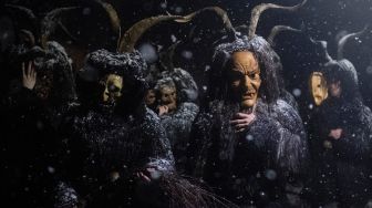 Orang-orang mengenakan topeng setan dan kulit domba hitam yang mewakili Krampus, penolong Santo Nikolas saat menghadiri parade Santo Nikolas (Nikolospiel) di Bad Mitterndorf, Styria, Austria, Senin (5/12/2022). [JOE KLAMAR / AFP]