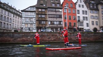 Para pendayung berpakaian Sinterklas menghadiri parade SUP (Stand Up Paddleboarding) di sungai Ill di Strasbourg, Prancis, Sabtu (3/12/2022). [SEBASTIEN BOZON/AFP]
