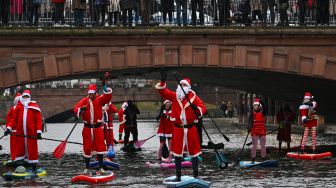 Pejalan kaki mengambil gambar saat para pendayung berpakaian Sinterklas menghadiri parade SUP (Stand Up Paddleboarding) di sungai Ill di Strasbourg, Prancis, Sabtu (3/12/2022). [SEBASTIEN BOZON/AFP]