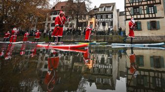Para pendayung berpakaian Sinterklas menghadiri parade SUP (Stand Up Paddleboarding) di sungai Ill di Strasbourg, Prancis, Sabtu (3/12/2022). [SEBASTIEN BOZON/AFP]
