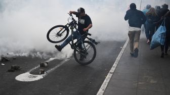 Orang-orang melindungi diri dari gas air mata yang dilemparkan polisi saat bentrok dengan pendukung mantan Presiden Peru Pedro Castillo di pinggiran Prefektur Lima tempat Castillo ditahan, di Lima, Peru, Rabu (7/12/2022). [ERNESTO BENAVIDES / AFP]
