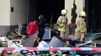 Seorang wanita membawa koper melewati puing-puing di depan hotel Radisson Blu, tempat akuarium besar yang terletak di lobi hotel meledak di Berlin, Jerman, Jumat (16/12/2022). [John MACDOUGALL / AFP]