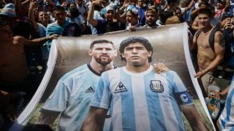 Fans Argentina membentangkan bendera bergambar bintang sepak bola Argentina Lionel Messi (kiri) dan Diego Maradona (kanan) saat berkumpul di Tugu Obelisk untuk merayakan kemenangan Piala Dunia Qatar 2022 melawan Prancis di Buenos Aires, Argentina, Minggu (18/12/2022). [Emiliano Lasalvia / AFP]