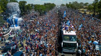 Para pemain Timnas Argentina melakukan selebrasi di atas bus dengan tanda bertuliskan "Juara Dunia" bersama pendukung setelah menjuarai turnamen Piala Dunia 2022 Qatar saat mereka melakukan tur keliling di pusat kota Buenos Aires, Argentina, Selasa (20/12/2022). [TOMAS CUESTA / AFP]