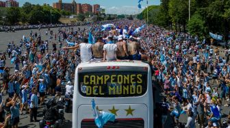 Para pemain Timnas Argentina melakukan selebrasi di atas bus dengan tanda bertuliskan "Juara Dunia" bersama pendukung setelah menjuarai turnamen Piala Dunia 2022 Qatar saat mereka melakukan tur keliling di pusat kota Buenos Aires, Argentina, Selasa (20/12/2022). [TOMAS CUESTA / AFP]
