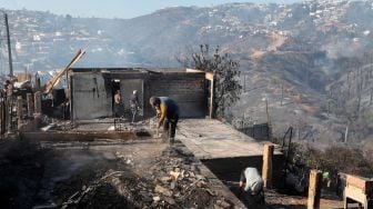 Para pria memindahkan puing-puing dari rumah yang hancur akibat kebakaran hutan di perbukitan Vina del Mar, di Wilayah Valparaiso, Chili, Jumat (23/12/2022). [JAVIER TORRES/AFP]