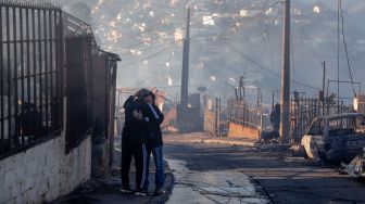 Orang-orang berpelukan di antara puing-puing rumah yang hancur akibat kebakaran hutan di perbukitan Vina del Mar, di Wilayah Valparaiso, Chili, Jumat (23/12/2022). [JAVIER TORRES/AFP]
