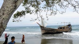 Warga menyaksikan kapal kayu menggunakan layar yang mengangkut puluhan imigran etnis Rohingya terdampar di pantai Desa Ladong, Kabupaten Aceh Besar, Aceh, Minggu (25/12/2022). [ANTARA FOTO/Ampelsa].