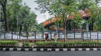 Pejalan kaki melintas di depan proyek pemasangan pagar di Tebet Eco Park, Tebet, Jakarta Selatan, Jumat (30/12/2022). [Suara.com/Alfian Winanto]