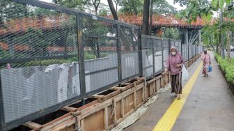 Pejalan kaki melintas di depan proyek pemasangan pagar di Tebet Eco Park, Tebet, Jakarta Selatan, Jumat (30/12/2022). [Suara.com/Alfian Winanto]