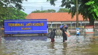 Warga berjalan melintasi Terminal Tipe A Jati yang tergenang banjir di Kudus, Jawa Tengah, Minggu (1/1/2023). [ANTARA FOTO/Yusuf Nugroho].