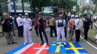 Massa yang tergabung dalam PA 212 injak bendera Belanda dan Swedia saat aksi di depan Kedutaan Besar (Kedubes) Swedia, Kuningan, Jakarta Selatan pada Senin (30/1/2023). [Suara.com/Yamual]