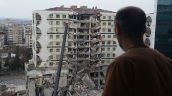 Seorang pria melihat operasi pencarian dan penyelamatan yang dilakukan di reruntuhan bangunan aakibat gempa bumi di Diyarbakir, Turki, Senin (6/2/2023). [ILYAS AKENGIN/AFP]
