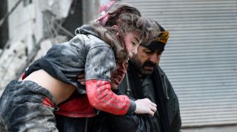 Warga membawa seorang anak yang terluka dari puing-puing bangunan yang runtuh setelah gempa bumi di kota Jandaris, provinsi Aleppo, Suriah, Senin (6/2/2023). [Rami al SAYED / AFP]
