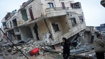 Warga berdiri di depan bangunan yang runtuh setelah gempa bumi di kota Jandaris, ddi kota Jandaris, provinsi Aleppo, Suriah, Senin (6/2/2023). [Rami al SAYED / AFP]
