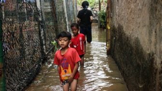 Anak-anak berjalan melewati banjir di kawasan pemukiman penduduk, Rawajati, Jakarta Selatan, Senin (27/2/2023). [Suara.com/Alfian Winanto]