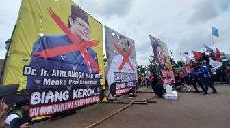 Massa tolak Perppu Cipta Kerja membawa baliho besar bergambar wajah 3 menteri di pemerintahan Joko Widodo, pada Selasa (14/3/2023). Mereka aksi di depan gedung DPR RI, [Suara.com/Faqih]