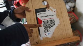 Seorang jemaah menunjukkan sisa stiker kode QRIS palsu pada kotak amal yang dipasang oleh oknum warga di Masjid Nurul Iman Blok M Square, Jakarta, Selasa (11/4/2023). [ANTARA FOTO/Aditya Pradana Putra].