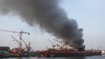 Petugas dengan menggunakan kapal tunda (tug boat) menyemprotkan air ke KM Anugerah Mandiri 8 yang terbakar di atas dok apung PT DOK dan Perkapalan Surabaya, Pelabuhan Tanjung Perak, Surabaya, Jawa Timur, Rabu (19/4/2023). [ANTARA FOTO/Didik Suhartono]