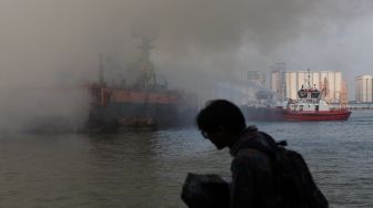 Petugas dengan menggunakan kapal tunda (tug boat) menyemprotkan air ke KM Anugerah Mandiri 8 yang terbakar di atas dok apung PT DOK dan Perkapalan Surabaya, Pelabuhan Tanjung Perak, Surabaya, Jawa Timur, Rabu (19/4/2023). [ANTARA FOTO/Didik Suhartono]